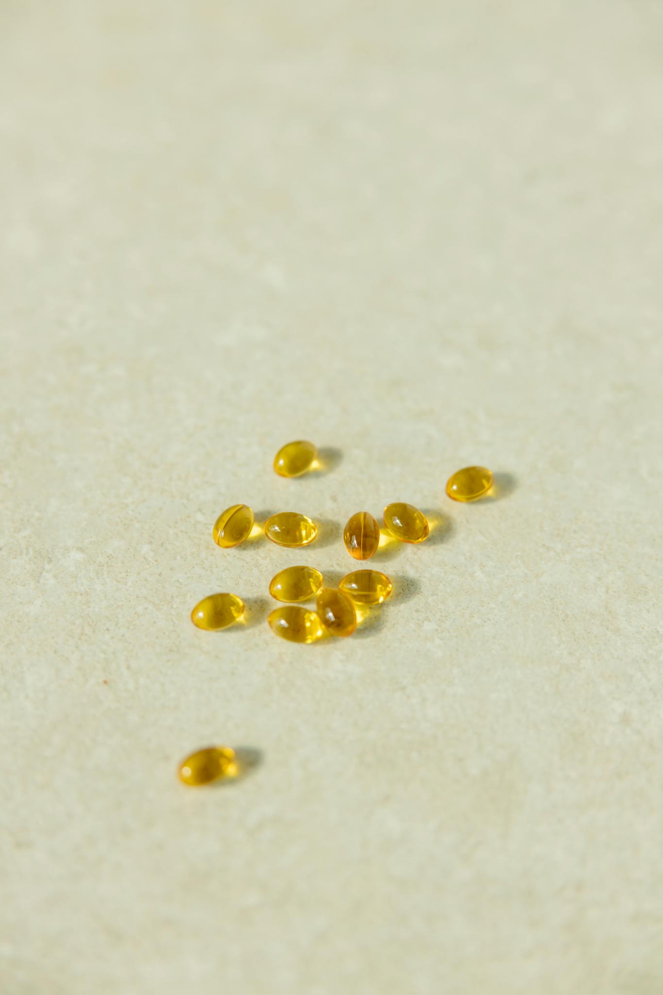 A collection of transparent golden capsules arranged on a neutral light background depicting supplements or vitamins.