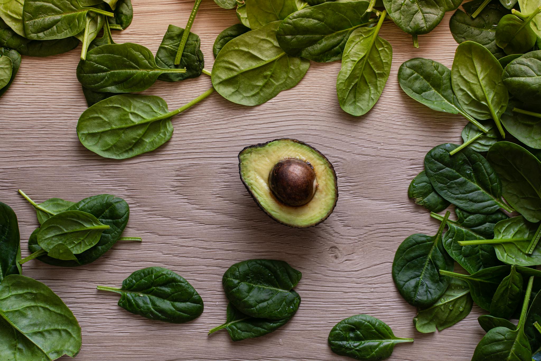 Flatlay of fresh avocado and spinach leaves on a wooden table, perfect for healthy eating concepts.